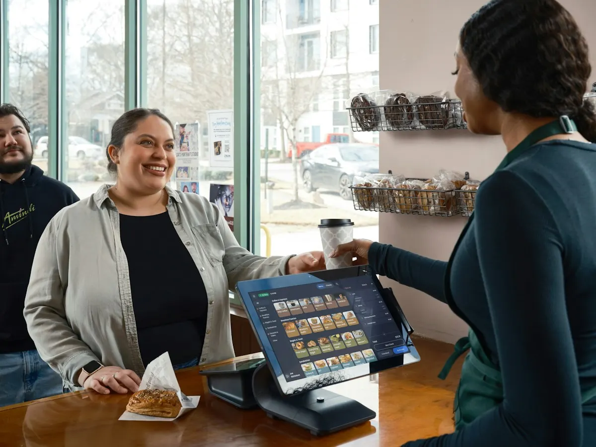 Smiling barista handing a coffee to a happy customer at the counter