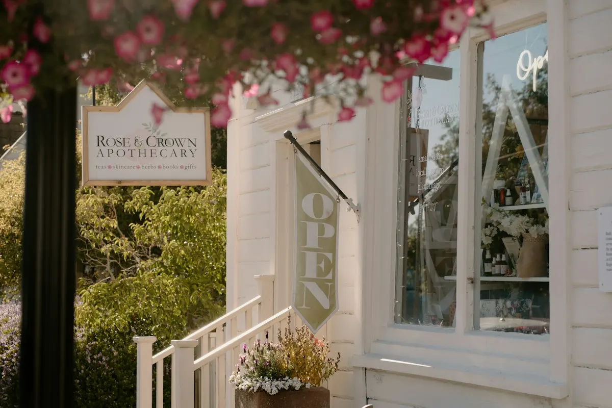 Small apothecary storefront with an open flag and flowers
